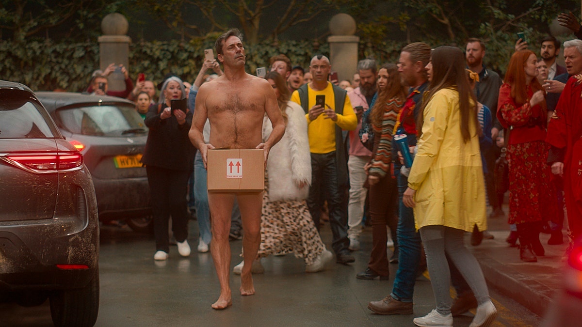 Jon Hamm walking naked with a box covering his private parts in Good Omens