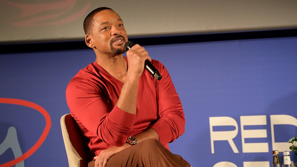 Will Smith sits on stage with a microphone
